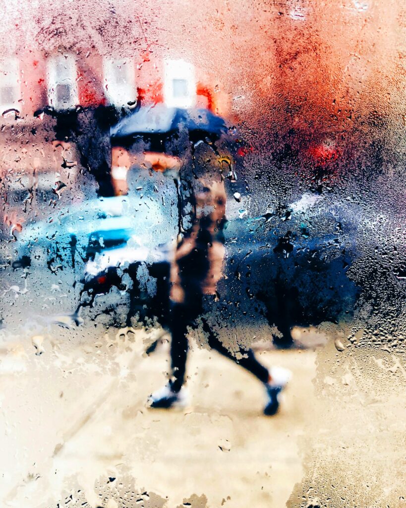 Blurry figures walking in the rain, condensation forming on a window.