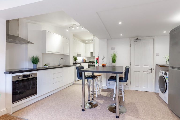 Modern double kitchen and dining area at 24 Granville Street, Cheltenham GL50 4BL, with a central bar and stools, fridge and heat pump tumble dryer