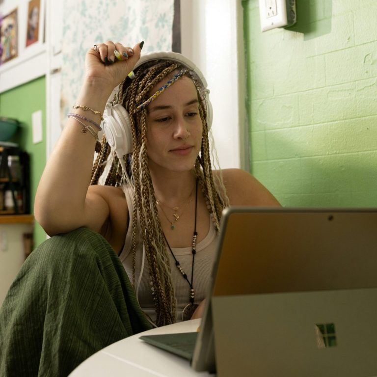 Woman with dreadlocks using a laptop while seated on a chair..