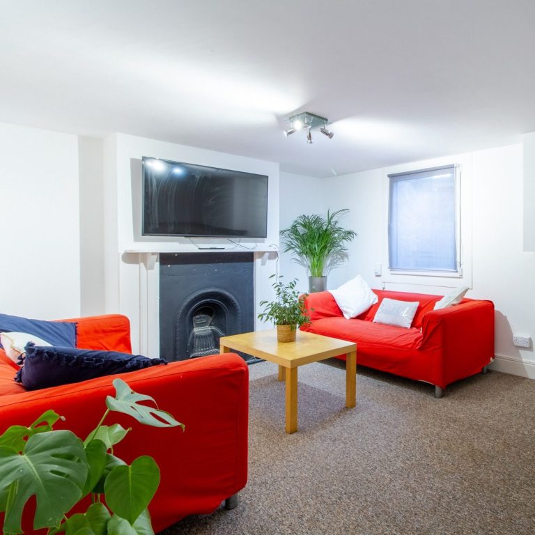 Living room with red sofas and a large TV at 5 St Pauls Street North, Cheltenham